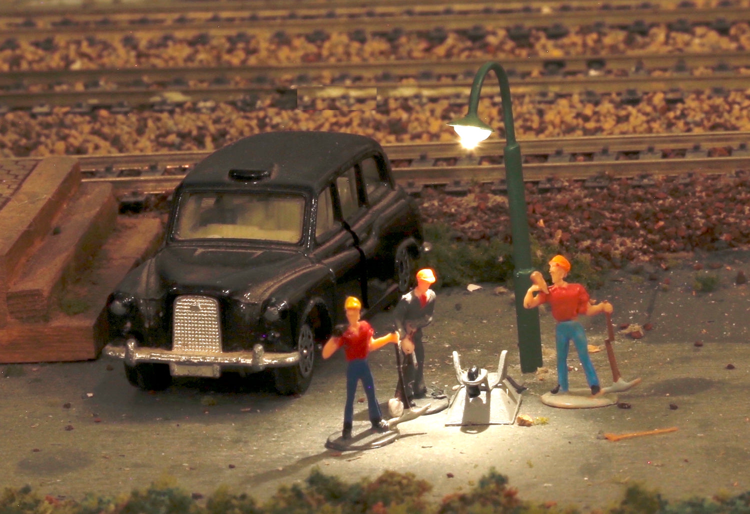 Gooseneck lamp highlights men digging up road on model train layout